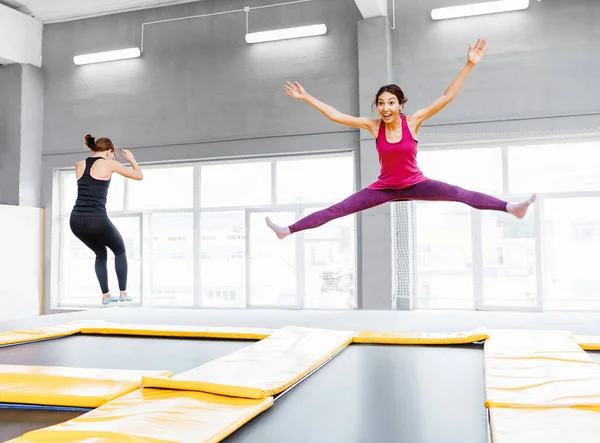 Dos jóvenes amigas saltando en un trampolín y haciendo split en el interior — Foto de Stock