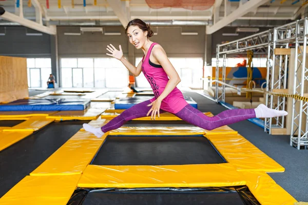 Mujer alegre y feliz practicando y saltando en camas elásticas en un centro deportivo cubierto, entrenamiento y concepto de entretenimiento moderno — Foto de Stock