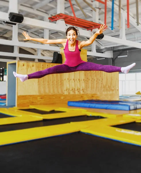 Молодая женщина акробатическая спортсменка прыжки и упражнения на батуте в помещении, современное хобби и фитнес-концепция — стоковое фото