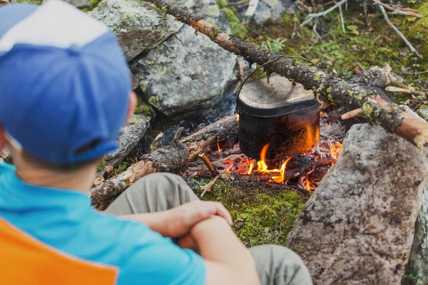 Giovane ragazzo cucina cibo campo in calderone sul fuoco aperto — Foto Stock