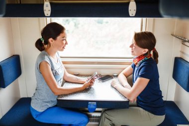 Two women Friends talking and laughing while traveling by reserved ticket train, railroad trip concept clipart