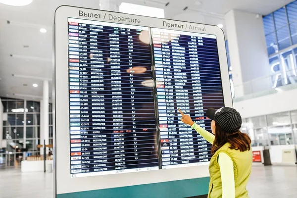 09 SEPTEMBER 2017, KURUMOCH KUF AIRPORT, SAMARA, RUSSIA: Rear view of a beautiful young woman standing and looking at electronic scoreboard with a schedule of flights in airport — Stock Photo, Image