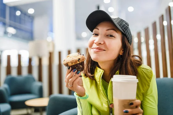 Молода брюнетка п'є каву та їсть смачний кекс у кафе сучасних аеропортів, концепція швидкого харчування — стокове фото
