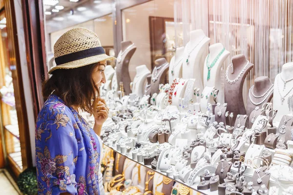 Vrouw in de hoed op zoek naar etalage of winkel venster en kiest een sieraden zilver luxe — Stockfoto
