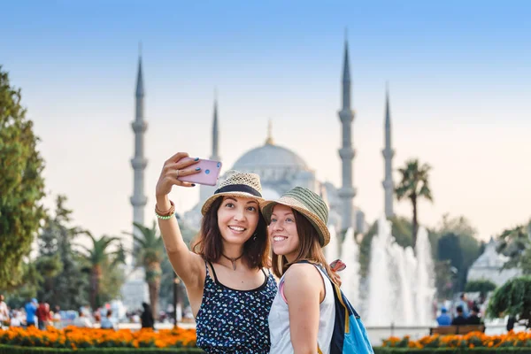 Две улыбающиеся девушки со смартфоном делают селфи перед Голубой мечетью в Стамбуле. Путешествия и отдых в Турции — стоковое фото