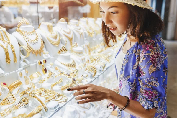 Žena v klobouku hledá showcase nebo obchod okna a zvolí luxusní zlaté šperky — Stock fotografie