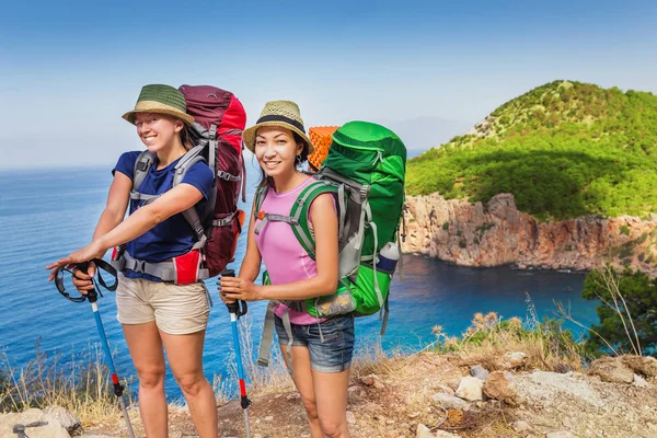 Two happy woman hikers friends with backpacks walking the Lycian Way and take a rest in an solitary lagoon with splendid view on a Mediterranean sea — Stock Photo, Image