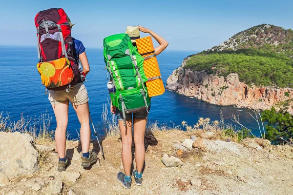 Two happy woman hikers friends with backpacks walking the Lycian Way and take a rest in an solitary lagoon with splendid view on a Mediterranean sea — Stock Photo, Image