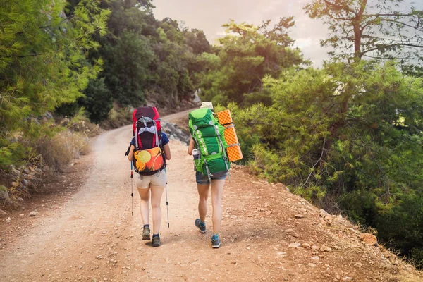 Back view of two female hikers with backpacks walking along an empry rural road — Stock Photo, Image