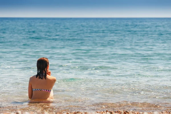 Mujer joven sentada en la playa en el mar, vista trasera — Foto de Stock