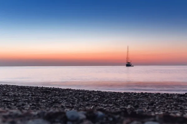 Сутінки перед світанком зі спокійним морем з силуетом яхти — стокове фото