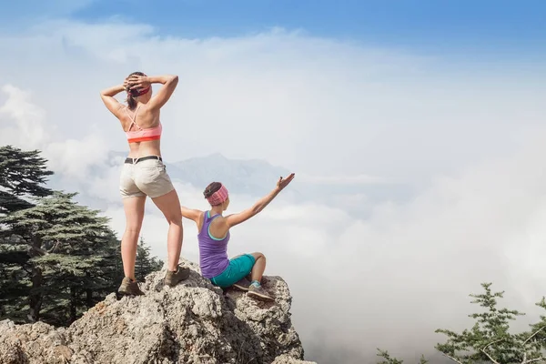 Dos mujeres se paran en la cima de la montaña por encima de las nubes y la niebla y están felices de la vista alfarera de las montañas de Tauro cerca del pico de Tahtali, Lycian Way — Foto de Stock