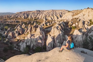 Bir dağın tepesinde oturan ve kırmızı Valley Kapadokya'da güneş doğarken arayan genç bir turist. Turizm ve seyahat Türkiye kavram