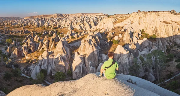 Um jovem turista sentado no topo de uma montanha e olhando para o nascer do sol na Capadócia no vale vermelho. Turismo e viagens na Turquia conceito — Fotografia de Stock