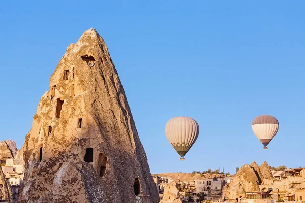 Hot air balloon flying over cave town and rocky cliffs of Cappadocia, one of the main tourist attraction of Turkey at sunset — Stock Photo, Image