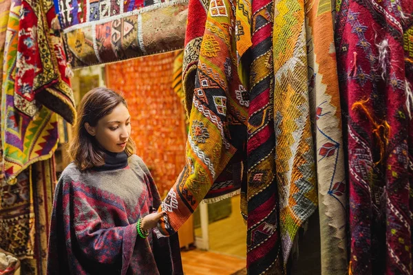 Молодая женщина Шоппинг для нового традиционного восточного пончо или ковер на туристическом рынке в Каппадокии. Ближневосточная концепция моды и одежды — стоковое фото