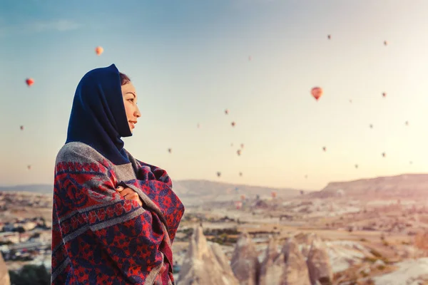 Žena v šatech tradiční pončo sledovat nádherný výhled na Barevné horkovzdušné balóny létání nad údolím v regionu Kapadocie, Turecko. — Stock fotografie
