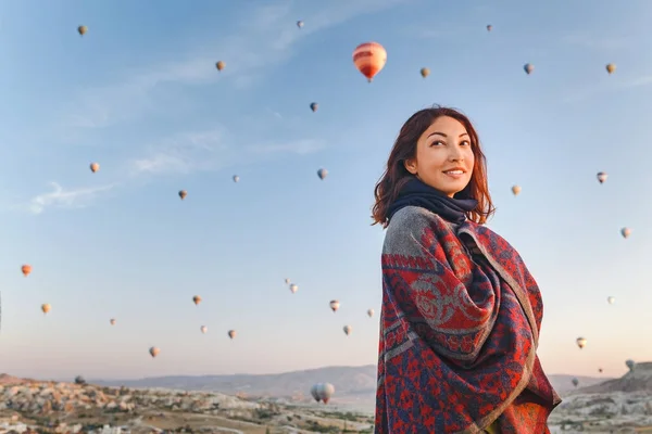 Kobieta w tradycyjnym Ponczo ubrania oglądać wspaniały widok, kolorowe balony latające nad doliną w regionie Kapadocja, Turcja. — Zdjęcie stockowe