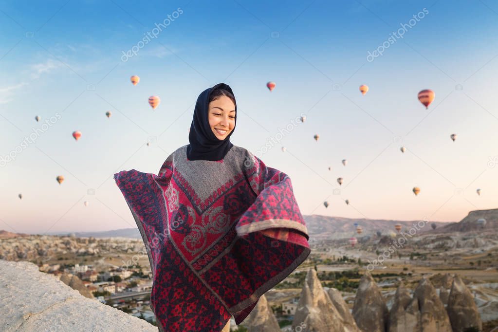 Woman in traditional poncho clothes watching wonderful view of a colorful hot air balloons flying over the valley at Cappadocia, Turkey.