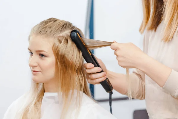 Endireitamento e ondulação de cabelo loiro no salão de penteado com ferro — Fotografia de Stock