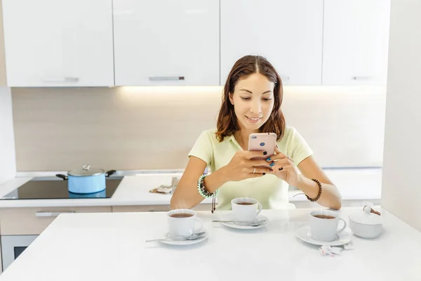 Casa joven y mujer de negocios en la cocina con teléfono inteligente y taza de té — Foto de Stock