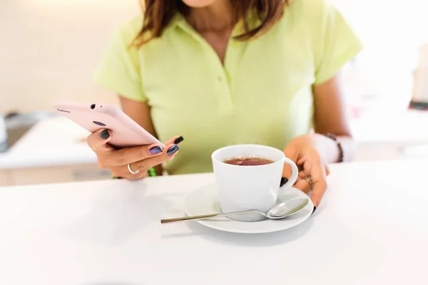 Молодая бытовая и деловая женщина на кухне со смартфоном и чашкой чая — стоковое фото