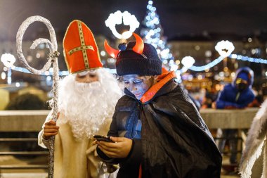 PRAGUE, CZECH REPUBLIC - DECEMBER 2017: Dressed in the costumes of devils and angels and St. Nicholas, children celebrate Christmas and have fun on the main square of the city clipart