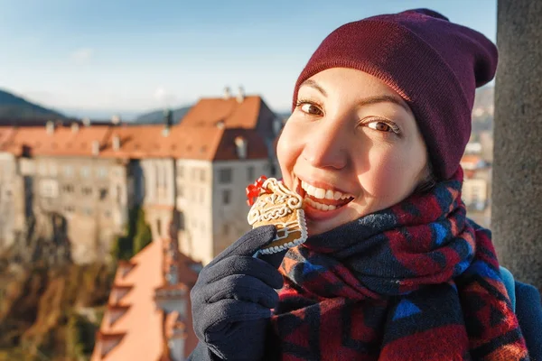 Menina segurando e comendo casa de gengibre no fundo da rua Chesky Krumlov decorado para o Natal — Fotografia de Stock