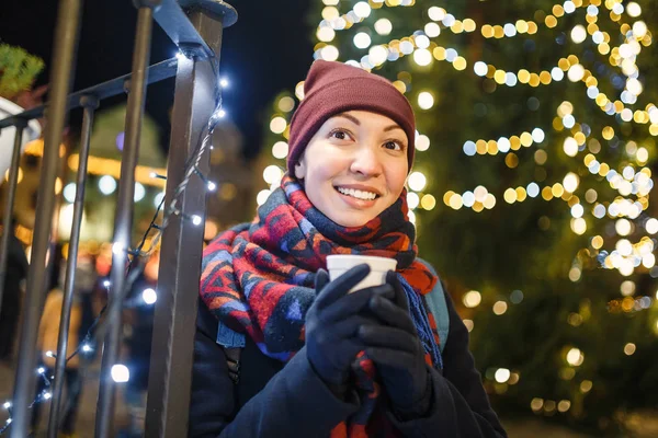 女性が新年のツリーの背景に熱いクリスマスの飲み物を飲む — ストック写真