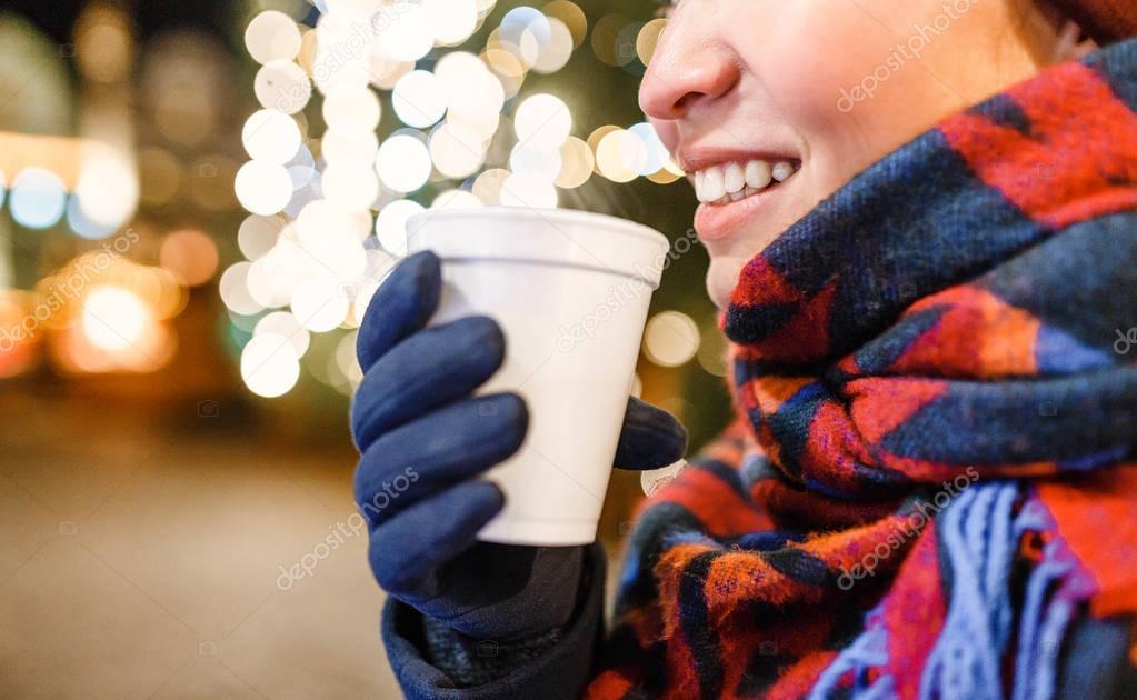 A woman drinks a hot Christmas drink on the background of a New Year tree
