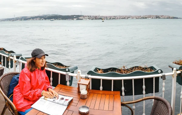 Женщина в ресторане с видом на море, глядя на меню — стоковое фото
