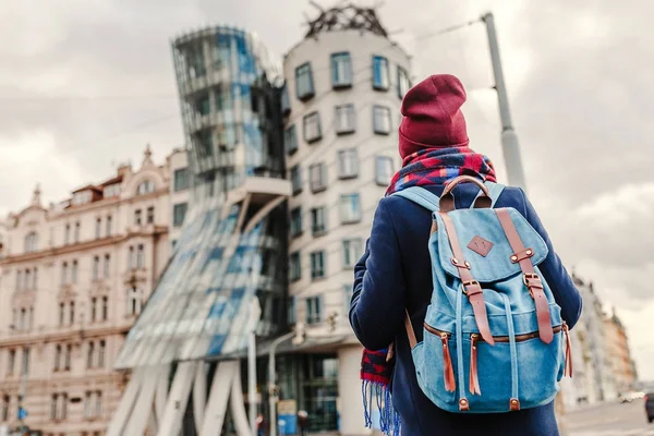 Mulher turista em um casaco com uma mochila viaja na Praga e olhando para a famosa Dancing House — Fotografia de Stock