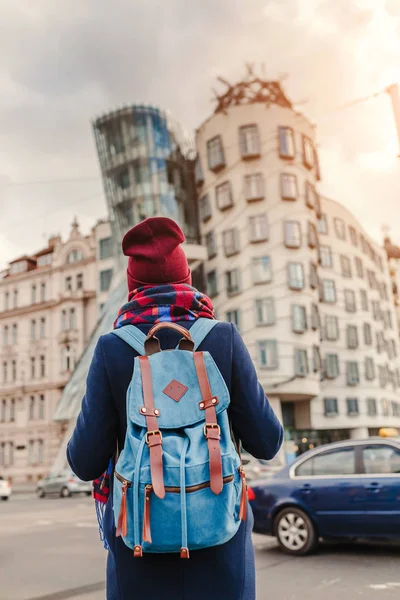 Mulher turista em um casaco com uma mochila viaja na Praga e olhando para a famosa Dancing House — Fotografia de Stock