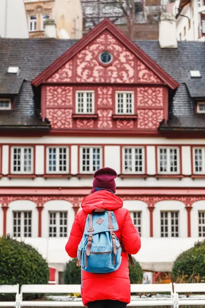 Visão traseira de uma mulher mochileira turística elegante olhando para um belo edifício arquitetônico em Carlsbad, República Checa — Fotografia de Stock