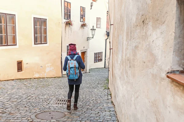 Kobieta turystycznych w płaszcz z plecakiem przemieszcza się na ulicach starego miasta Český Krumlov — Zdjęcie stockowe