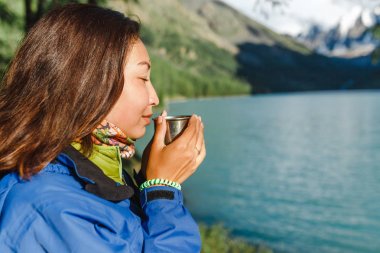 Uzun bir yürüyüş üzerinde bir dağ gölü yakınındaki güzel kokulu bir bitki çayı bir kız içecekler
