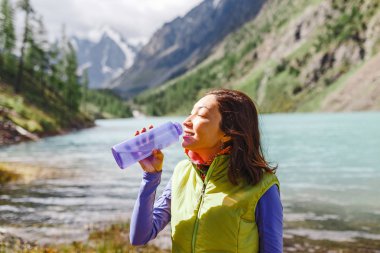 Bir gezgin kadın bir yürüyüş sırasında bir dağ dere taze suyu içer