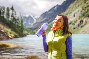 Bir gezgin kadın bir yürüyüş sırasında bir dağ dere taze suyu içer