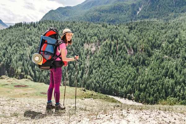 Joven mujer feliz con mochila caminando por el sendero solo en las montañas, el concepto de actividades al aire libre y aventuras en la naturaleza — Foto de Stock