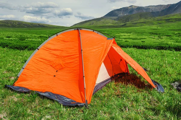 A bright orange tent is set on a beautiful lawn in the mountains, the concept of a relaxed outdoor recreation