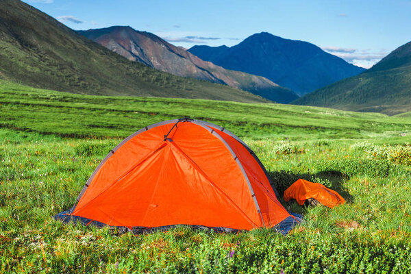 A bright orange tent is set on a beautiful lawn in the mountains, the concept of a relaxed outdoor recreation