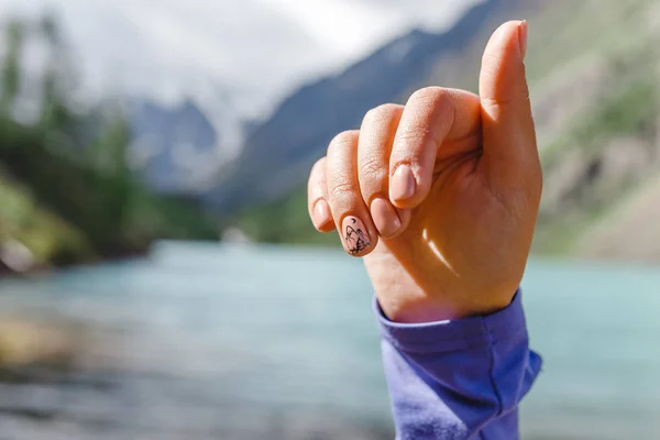 Drawing manicure on nails with a picture of mountains on the background of a lake