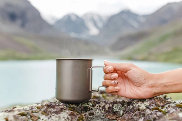 A girl drinks a fragrant herbal tea near a mountain lake on a hike — Stock Photo, Image