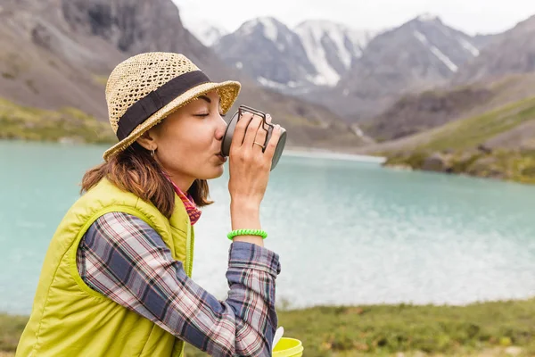 Дівчина п'є запашний трав'яний чай біля гірського озера під час походу — стокове фото
