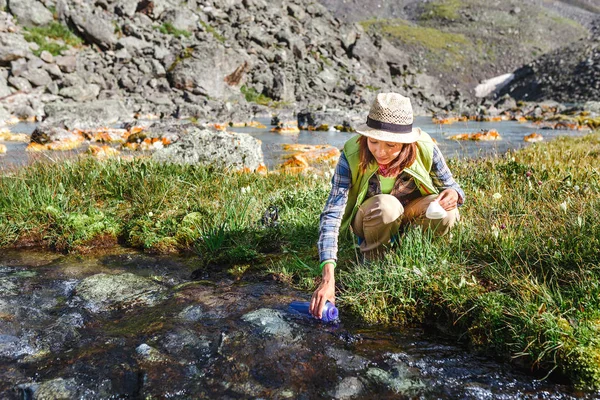 Женщина-путешественница пьет пресную воду из горного ручья во время похода — стоковое фото