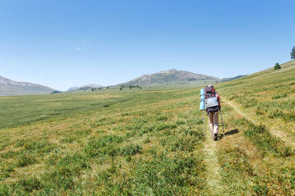 Joven mujer feliz con mochila caminando por el sendero solo en las montañas, el concepto de actividades al aire libre y aventuras en la naturaleza — Foto de Stock