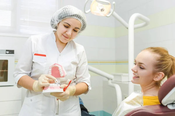 Una dentista donna sta curando i denti di una paziente e spiega come lavarsi i denti correttamente su un modello di mascella — Foto Stock