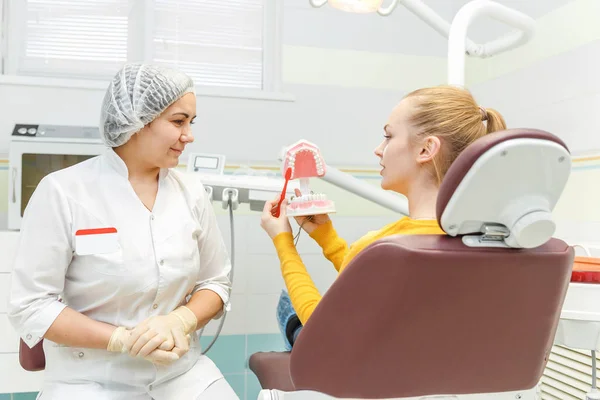 Uma dentista feminina está tratando os dentes de um paciente e explica como escovar os dentes corretamente em um mockup da mandíbula — Fotografia de Stock