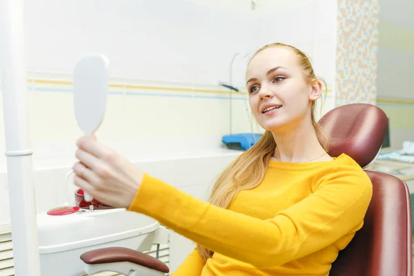 Giovane donna che controlla i denti allo specchio dopo il trattamento dentale in clinica di stomatologia — Foto Stock