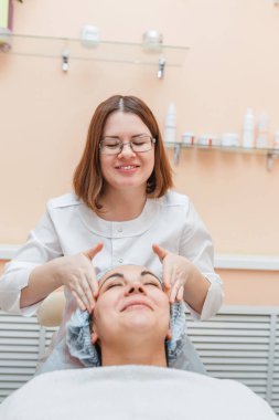 Kadın doktor bir kozmetik kliniğinde masajlar ve güzellik yordamına onu hazırlayarak istemcinin yüz temizler